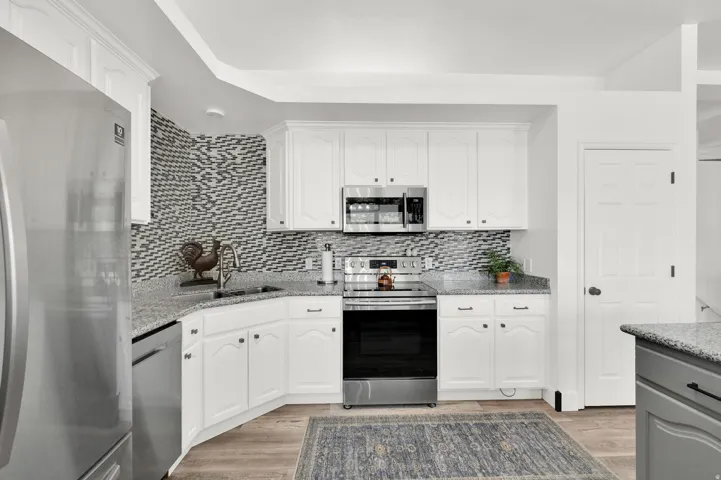 Kitchen featuring white cabinetry, stainless steel appliances, granite countertops, patterned tile backsplash, and wood-finish flooring