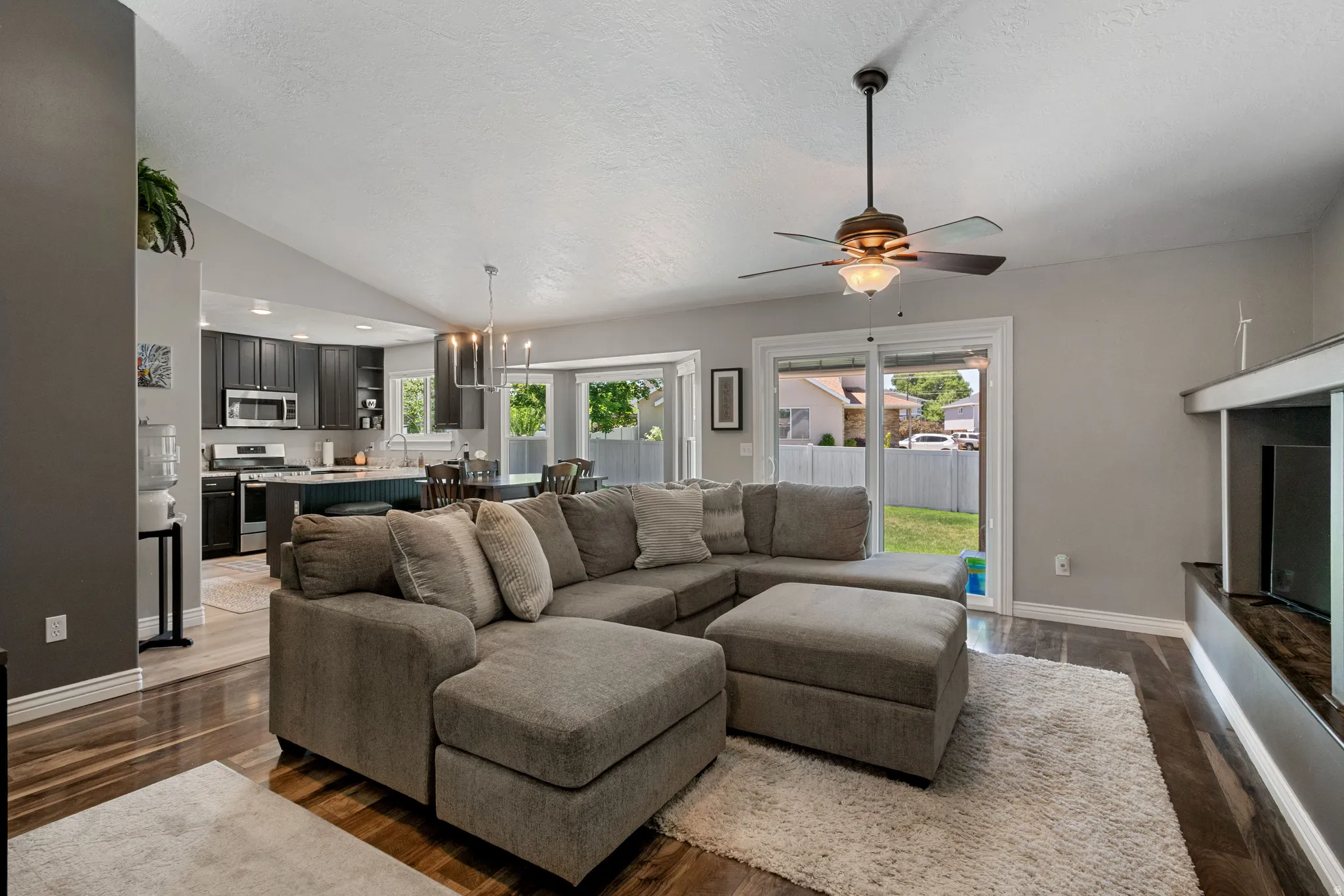Open-concept living area featuring wood-finish flooring, a vaulted ceiling, and a ceiling fan with integrated lighting