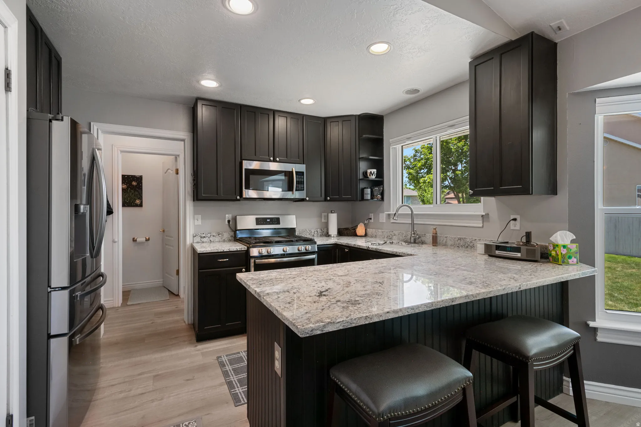 U-shaped kitchen featuring dark wood cabinetry, light-toned stone countertops, stainless steel appliances, recessed lighting, and wood-finish flooring