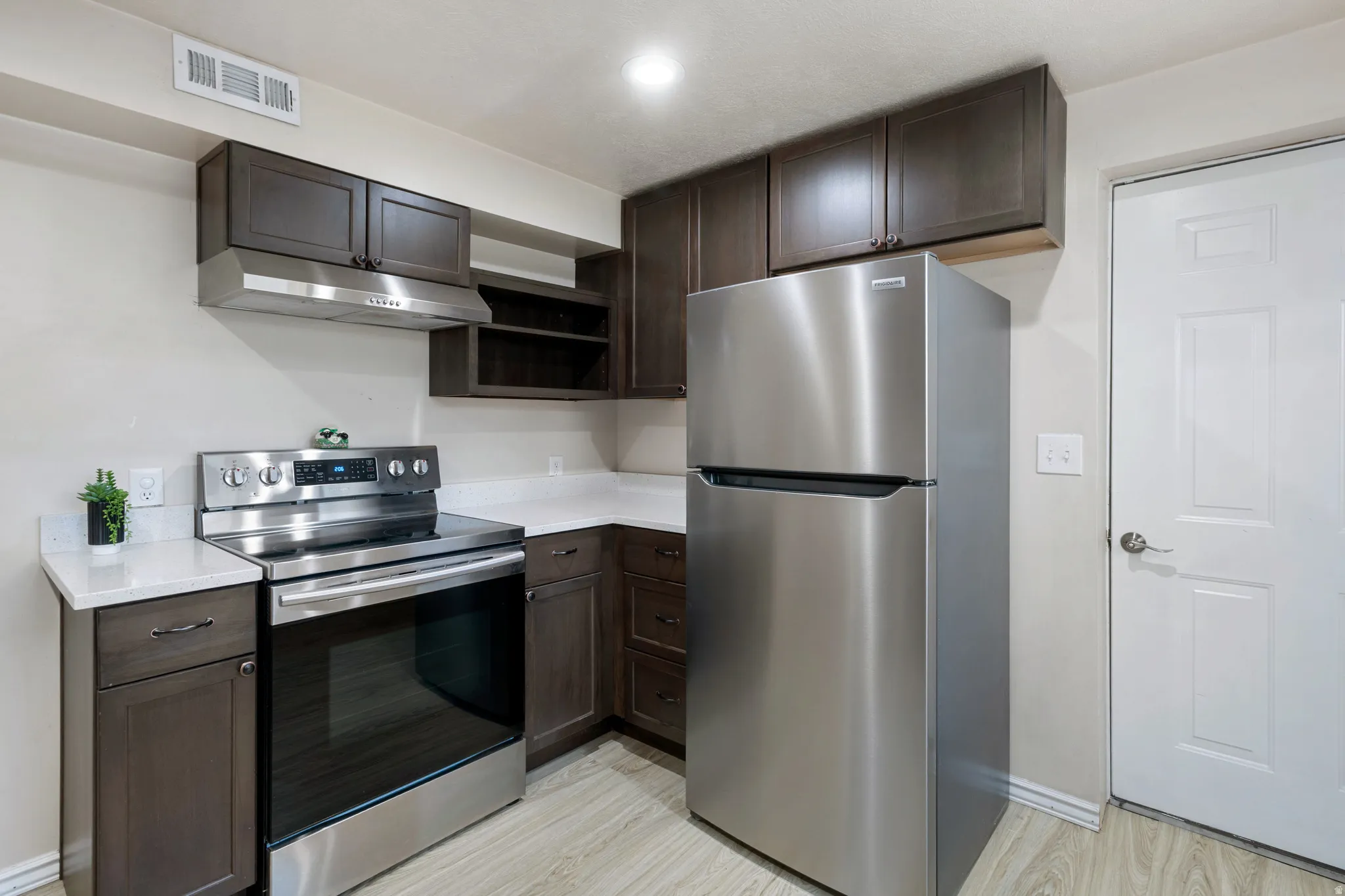 Kitchen featuring stainless steel appliances, dark wood-finish cabinetry, quartz countertops, and light wood-finish flooring