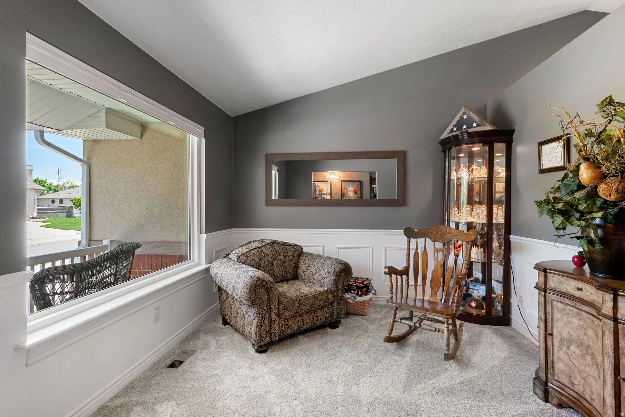 Carpeted interior space featuring a large picture window, dark gray walls with white wainscoting, and a corner display cabinet with interior lighting