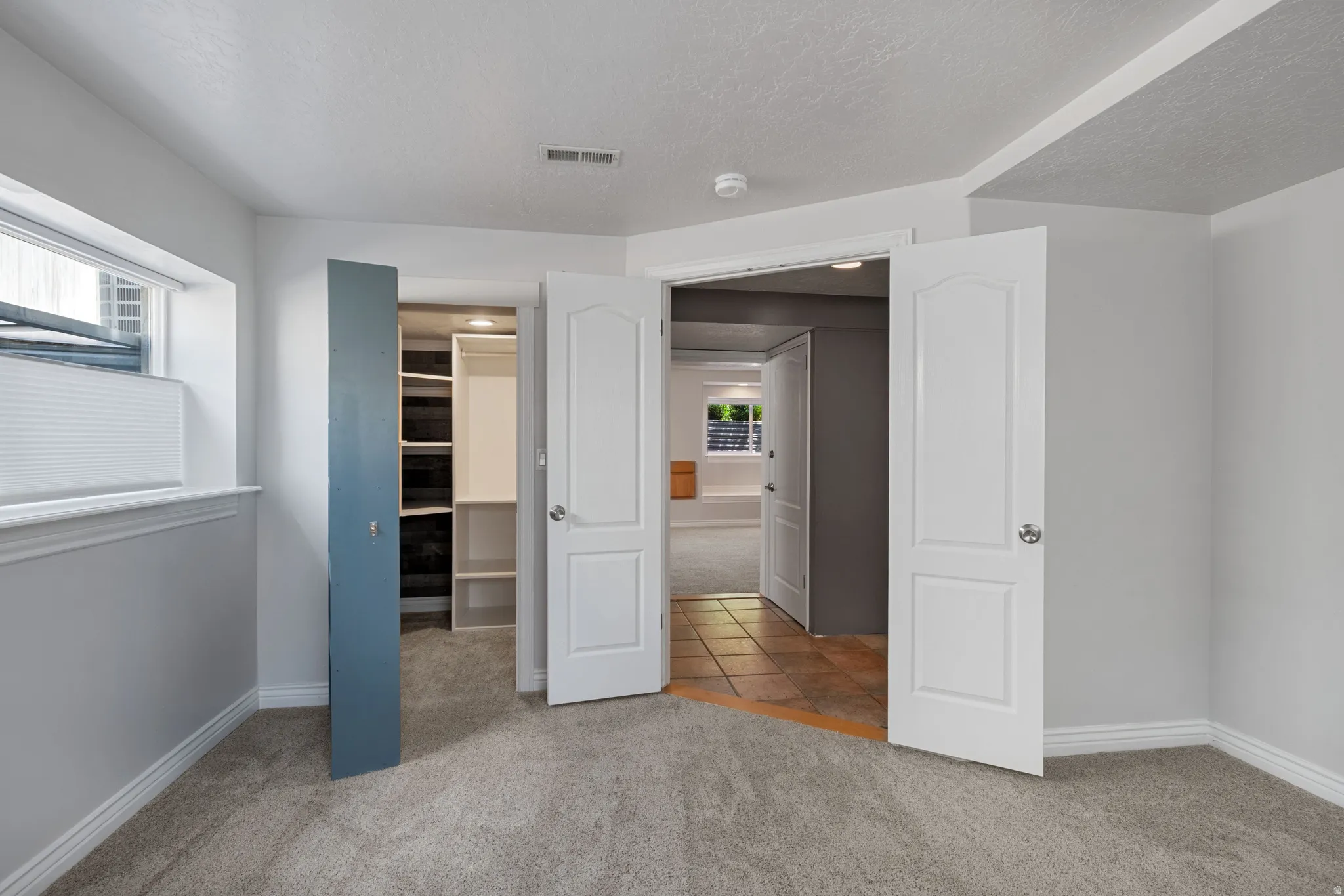 Carpeted room featuring a window with blinds, a bi-fold closet with shelving, and two panel doors