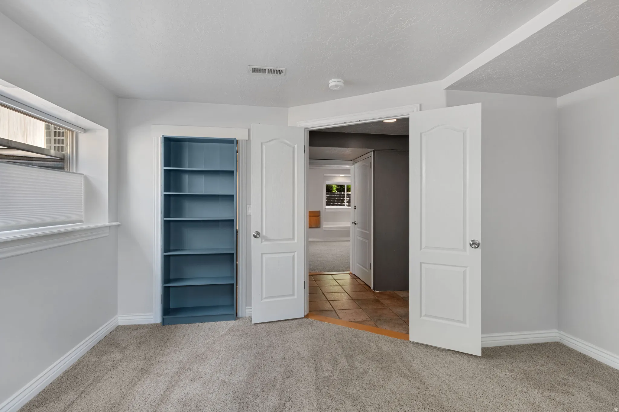 Carpeted room with a built-in blue shelving unit, a window with horizontal blinds, and a white trim package