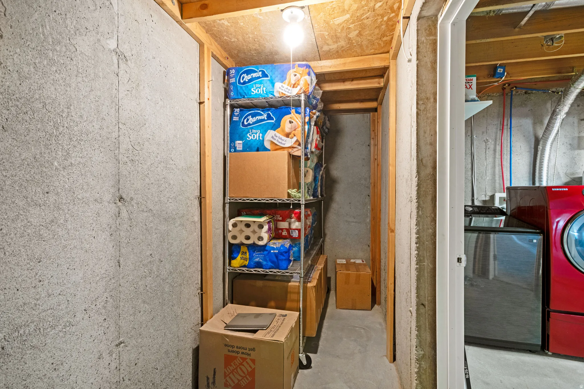 Unfinished basement area featuring concrete walls, exposed wood framing, and an overhead light fixture