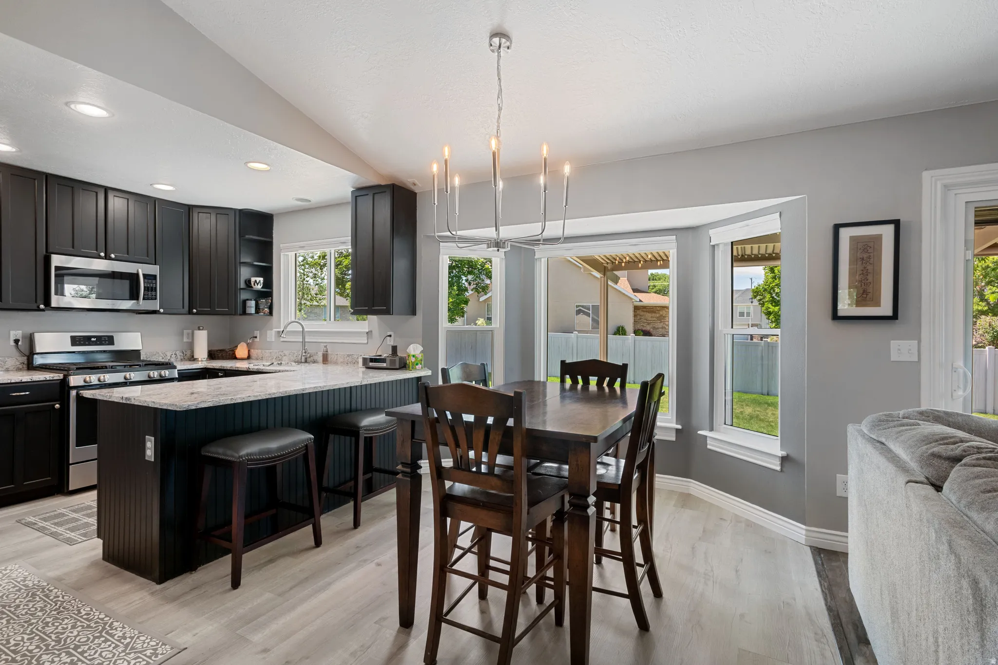 Open-concept kitchen and dining area featuring dark cabinetry, stainless steel appliances, and light-toned wood-finish flooring