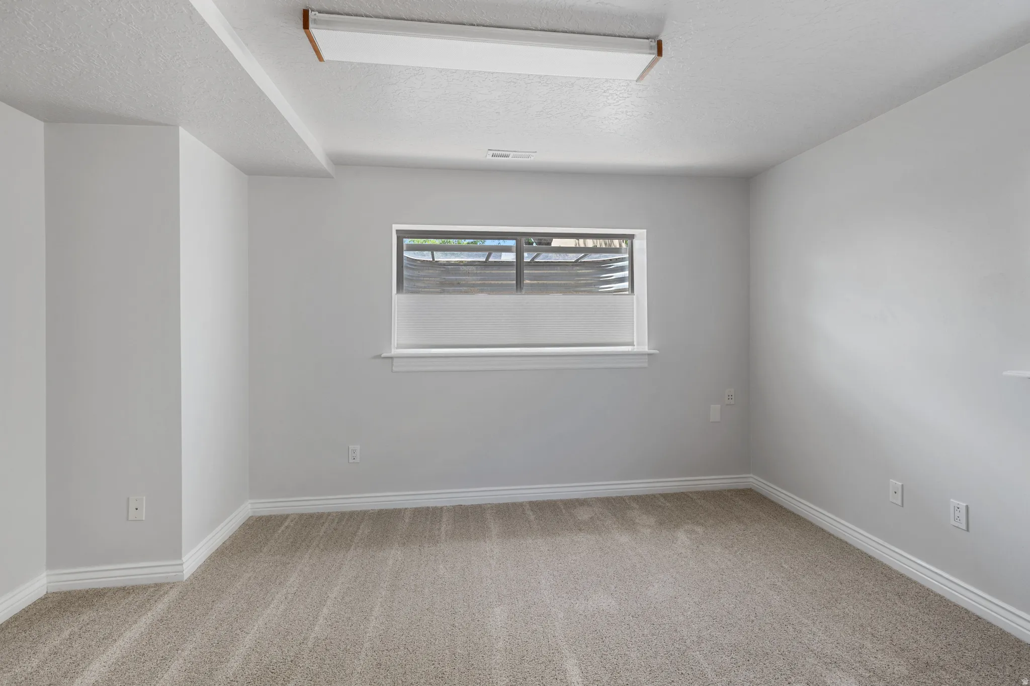 Carpeted room featuring a window with white trim, a flush-mount ceiling light fixture, and white baseboards