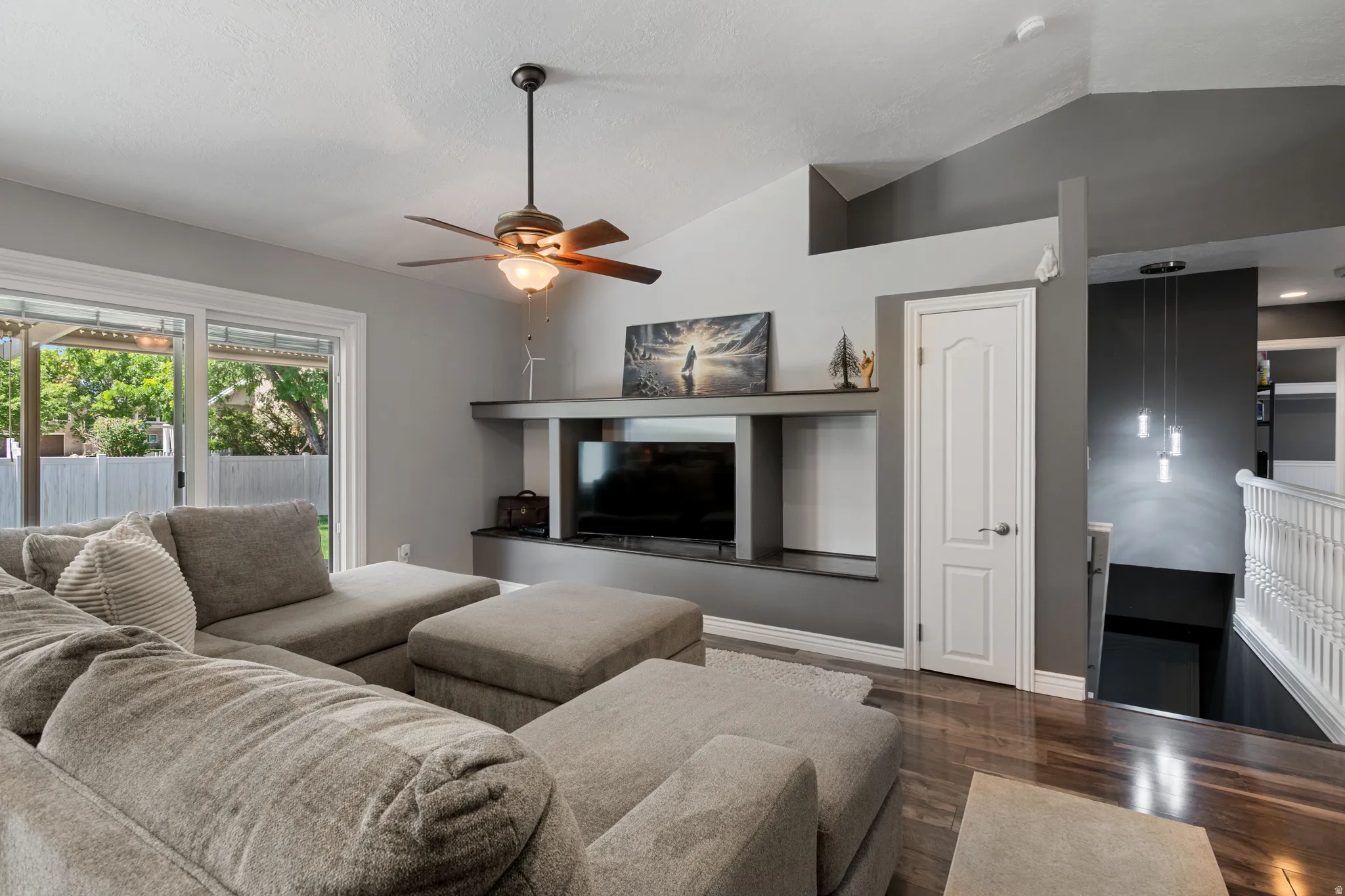 Living area featuring vaulted ceilings, a ceiling fan with integrated lighting, wood-finish flooring, a built-in media console, and sliding glass doors to the exterior