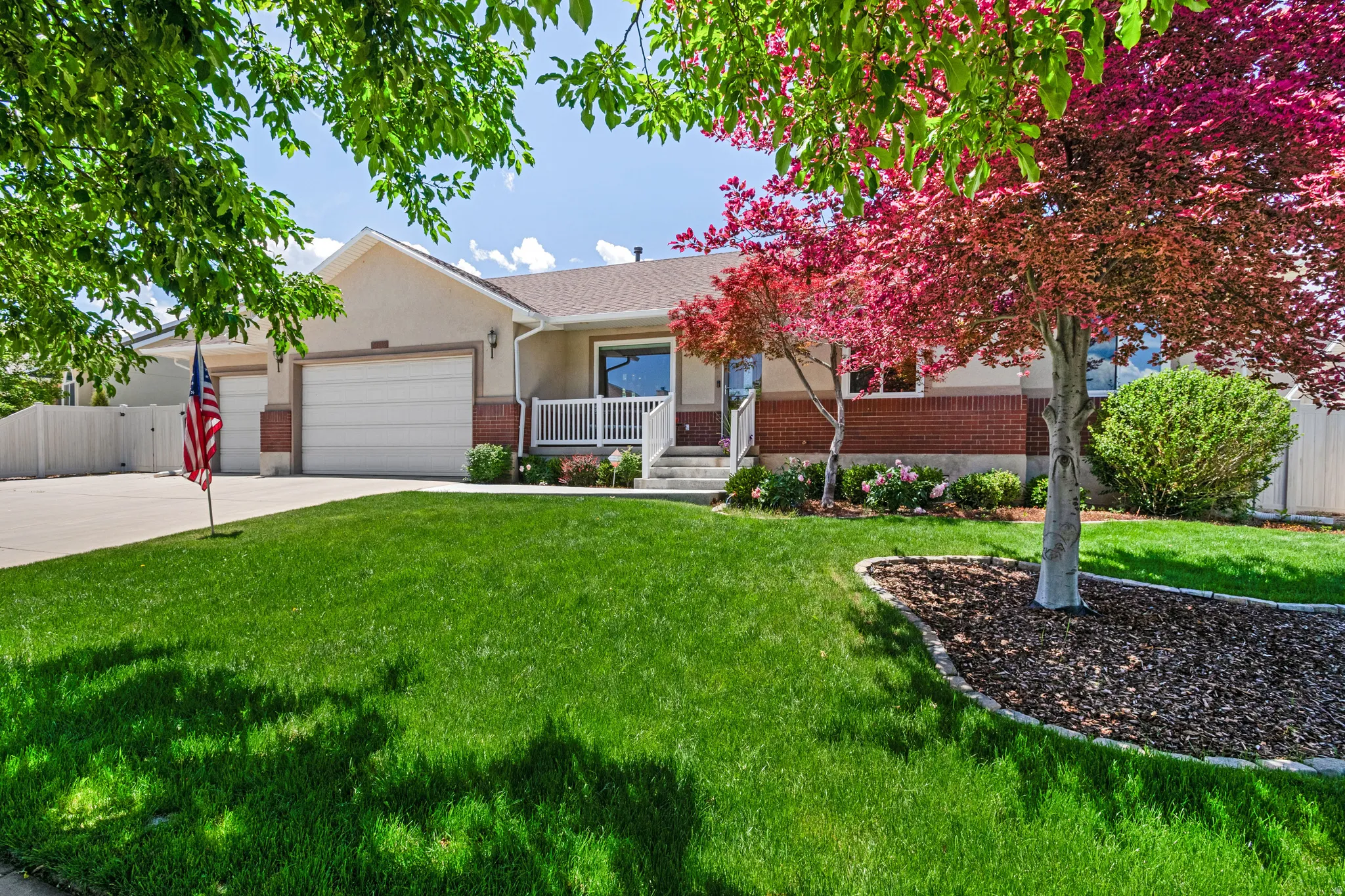 Stucco and brick exterior with a two-car garage, white porch railing, mature landscaping, and a manicured lawn