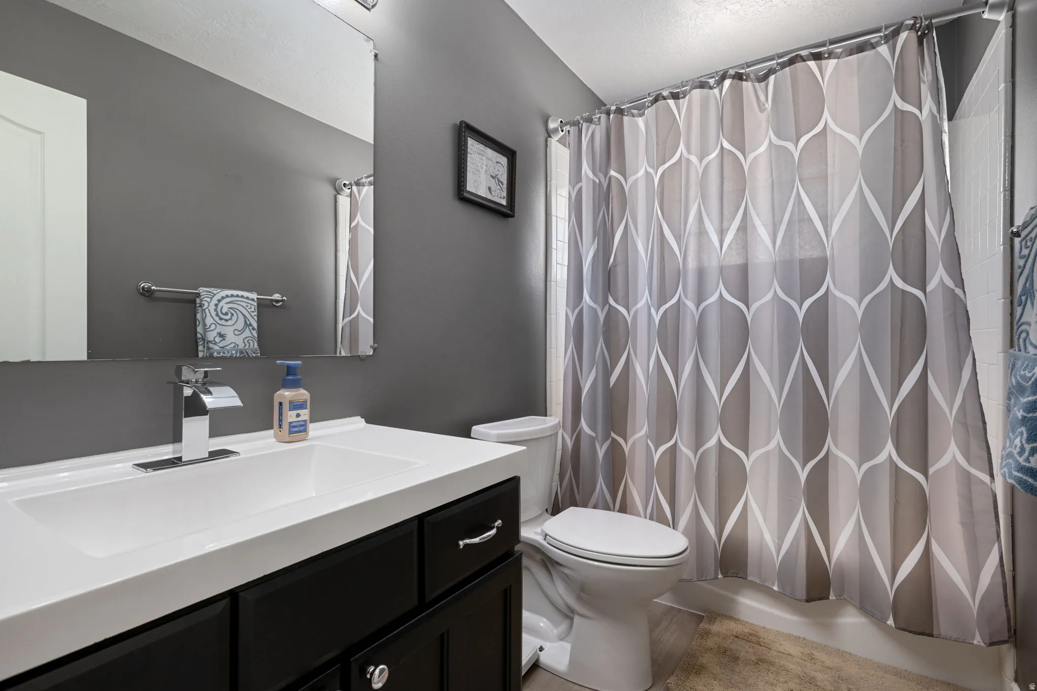 Bathroom featuring a dark gray wall, white vanity with integrated sink, chrome faucet, and a shower/tub combination with white subway tile surround