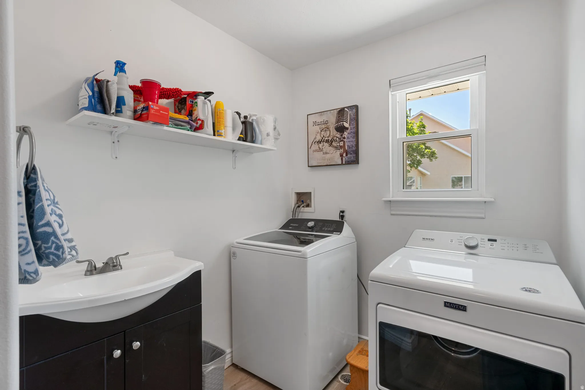 Laundry room featuring a single-pane window, wall-mounted shelving, a built-in sink with dark wood-finish cabinetry, and wood-finish flooring