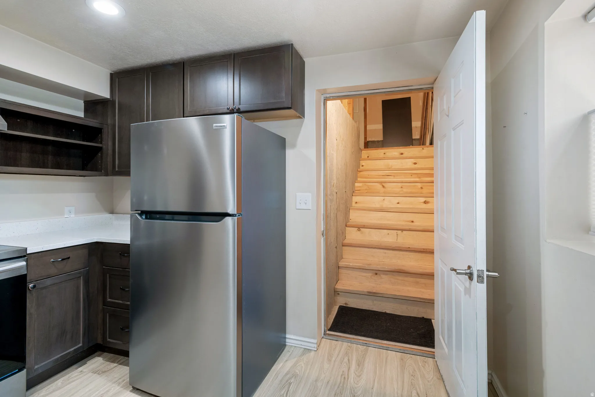 Kitchenette featuring dark wood-finish cabinetry, light-toned countertops, and a stainless steel refrigerator