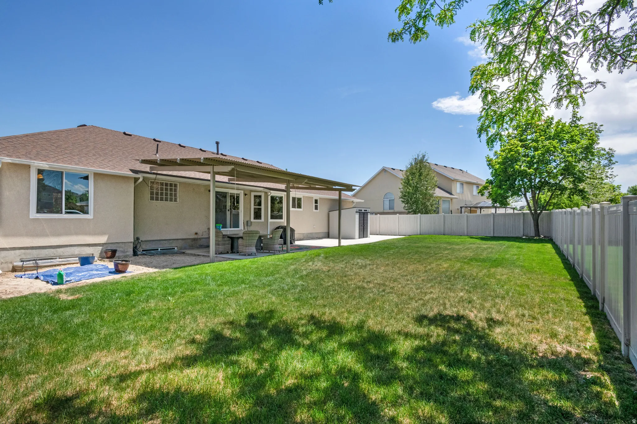 Expansive rear yard featuring a manicured lawn, full vinyl fencing, and a covered patio area