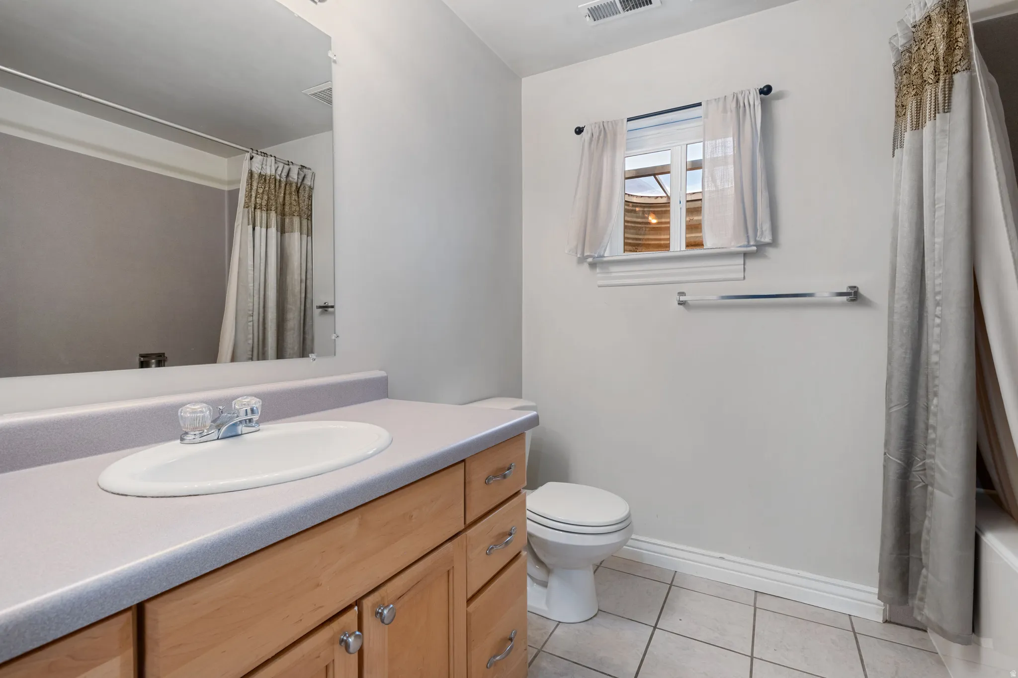 Bathroom featuring a light wood-finish vanity with an integrated sink, a large wall-mounted mirror, and tiled flooring