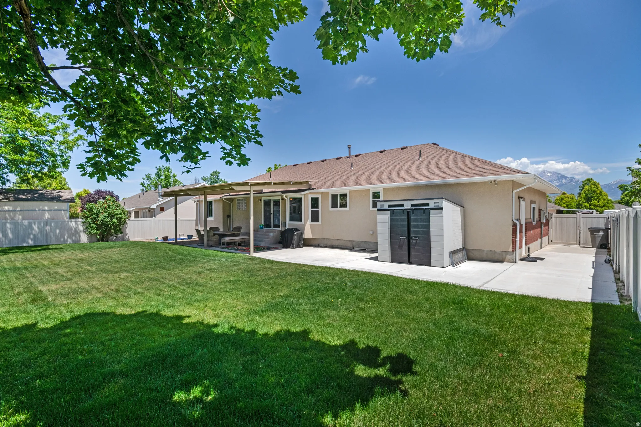 Expansive backyard featuring a large green lawn, covered patio, and concrete perimeter pathways