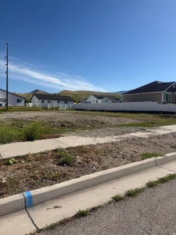Level building lot featuring a concrete curb, sidewalk, and partial fencing