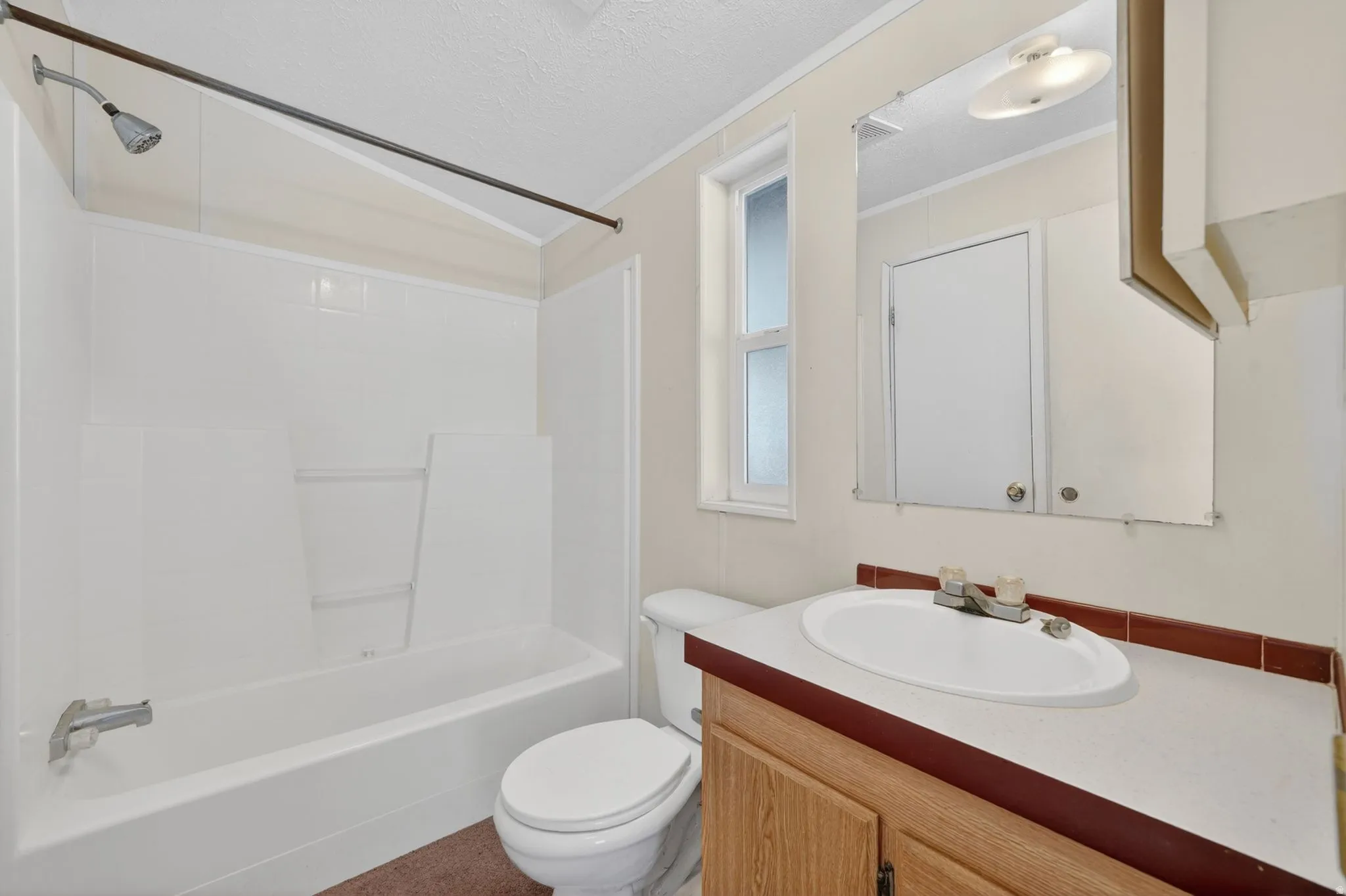 Bathroom featuring a white integrated tub and shower unit, wood-finish vanity with an oval sink, and a framed mirror