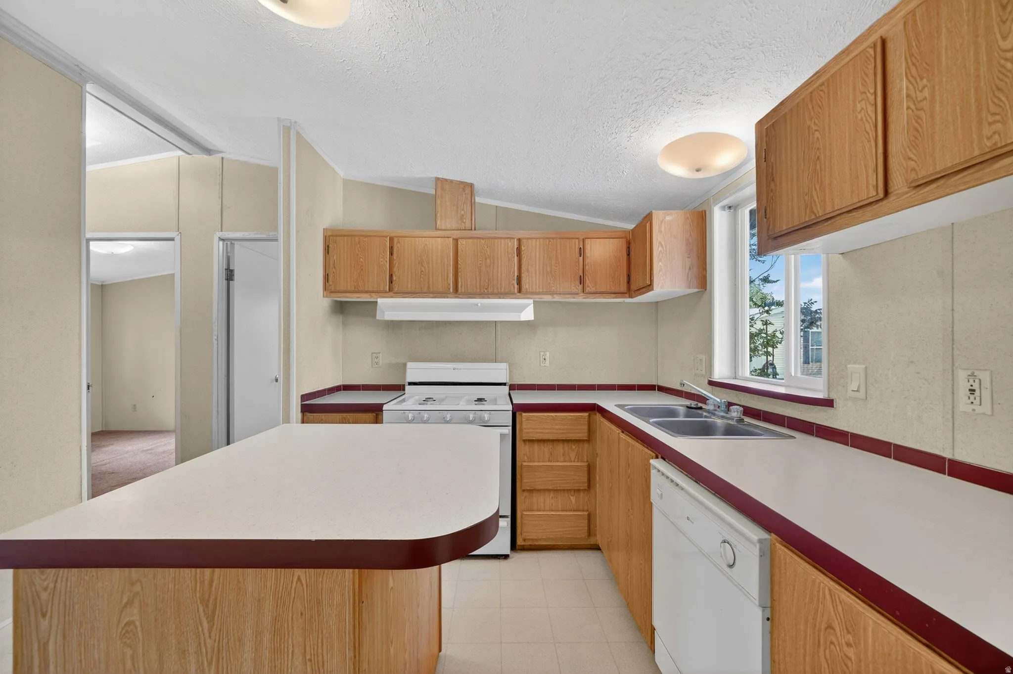 Kitchen featuring wood cabinetry, white countertops with red trim, a double basin sink, and a white dishwasher