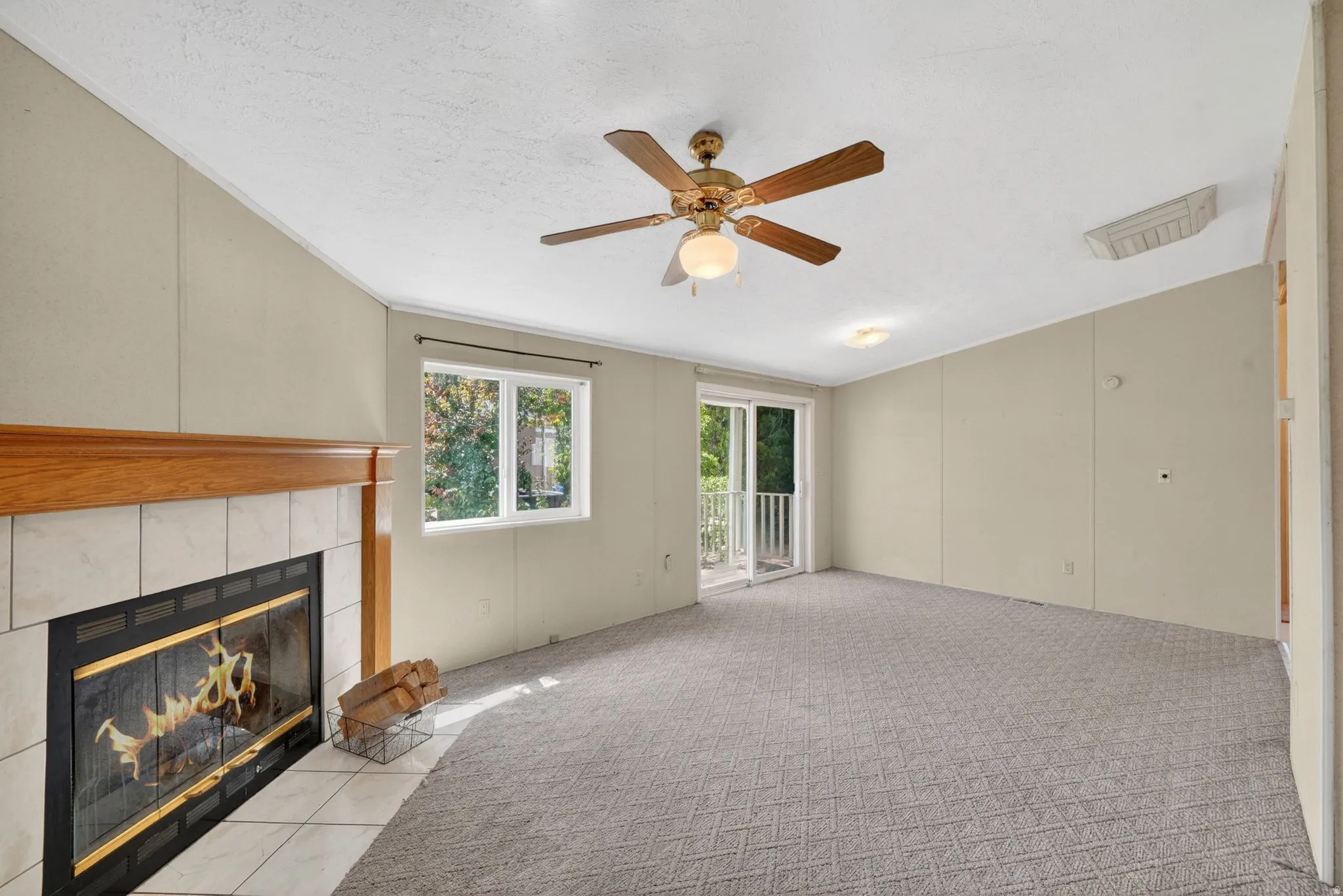 Spacious room featuring a fireplace with a tile surround and wood mantel, a ceiling fan, and carpeted flooring
