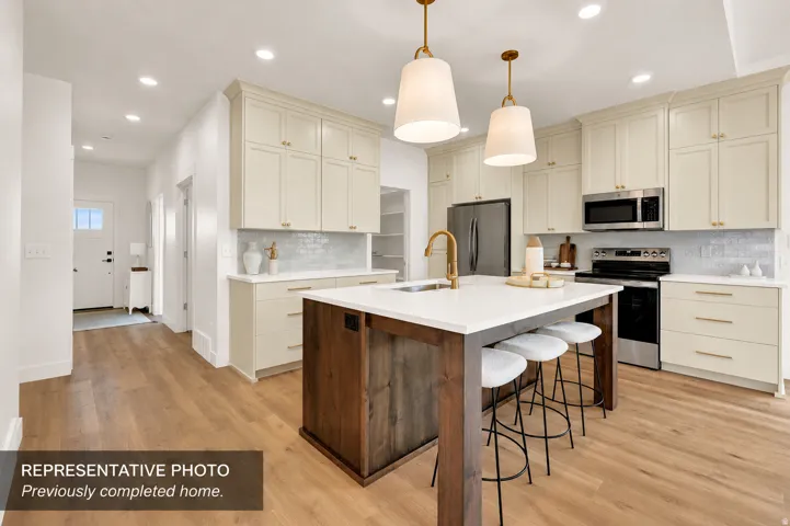 Modern kitchen featuring a large central island with seating, light-toned cabinetry, stainless steel appliances, and wood-finish flooring