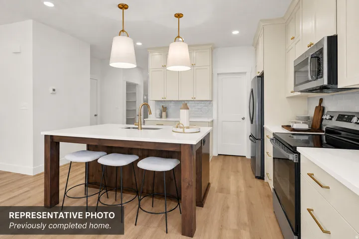 Kitchen featuring a large central island with seating, pendant lighting, stainless steel appliances, light-colored cabinetry with gold-toned hardware, and wood-finish flooring