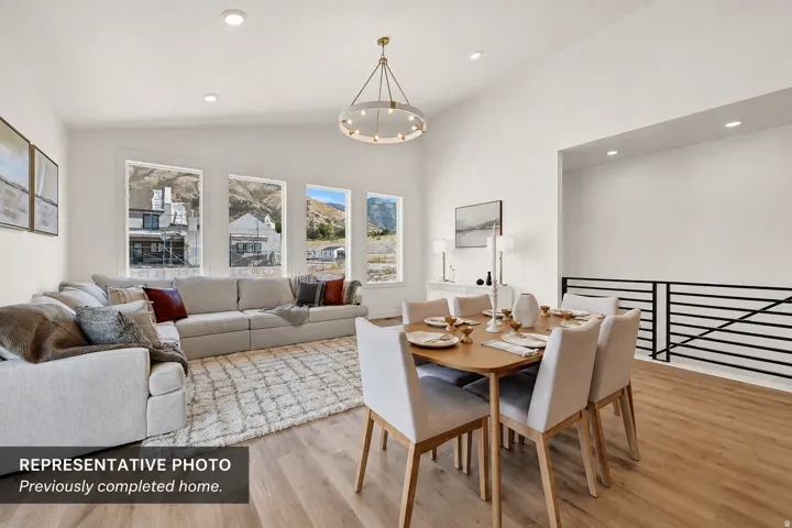 Vaulted ceiling living area featuring a contemporary chandelier, multiple windows with mountain scenery, wood-finish flooring, and a black horizontal slat railing