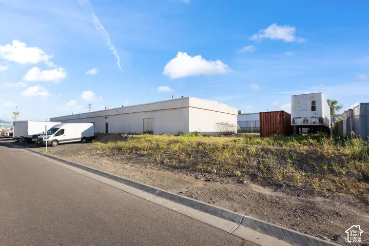 Industrial building featuring a light-colored exterior, multiple access doors, and an expansive paved lot