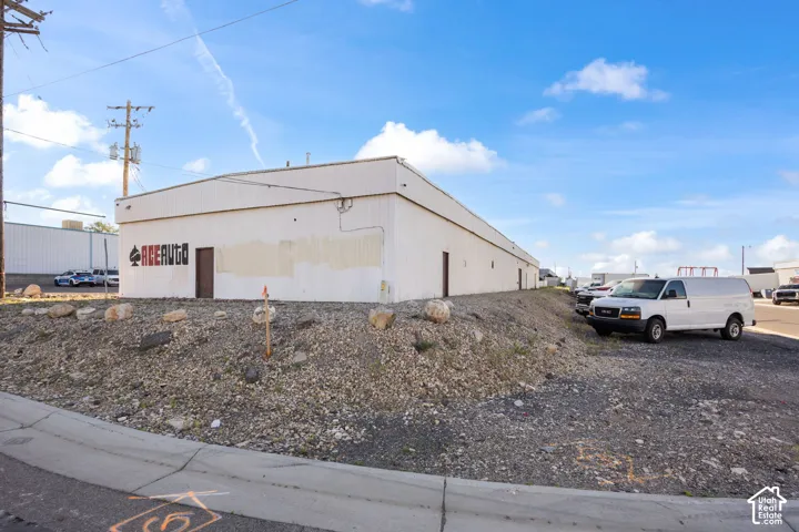 Commercial property featuring a large white industrial building with multiple entry points and an expansive gravel lot