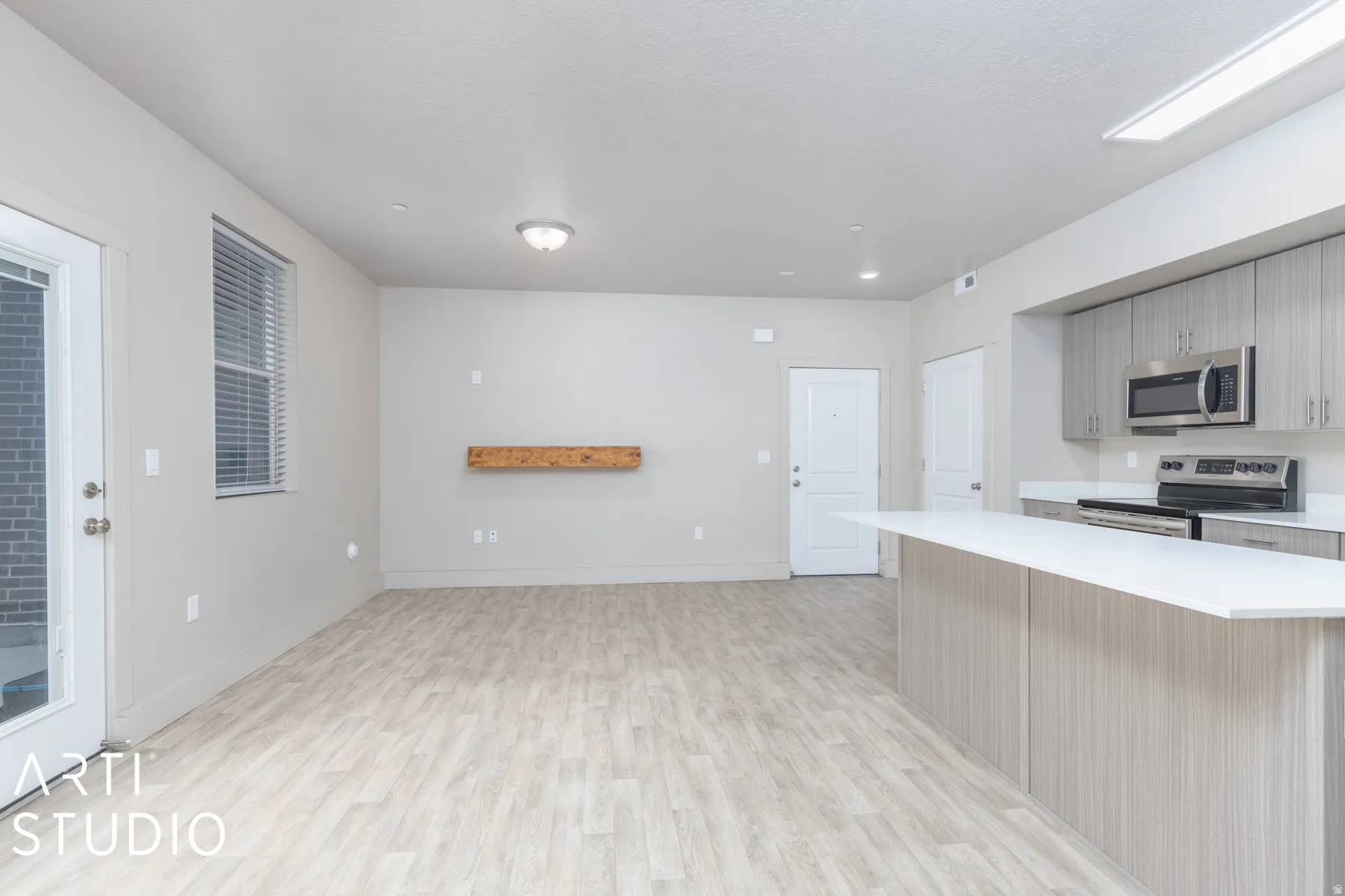 Open-concept living space featuring wood-finish flooring, a contemporary kitchen island with white countertop, recessed lighting, and stainless steel appliances
