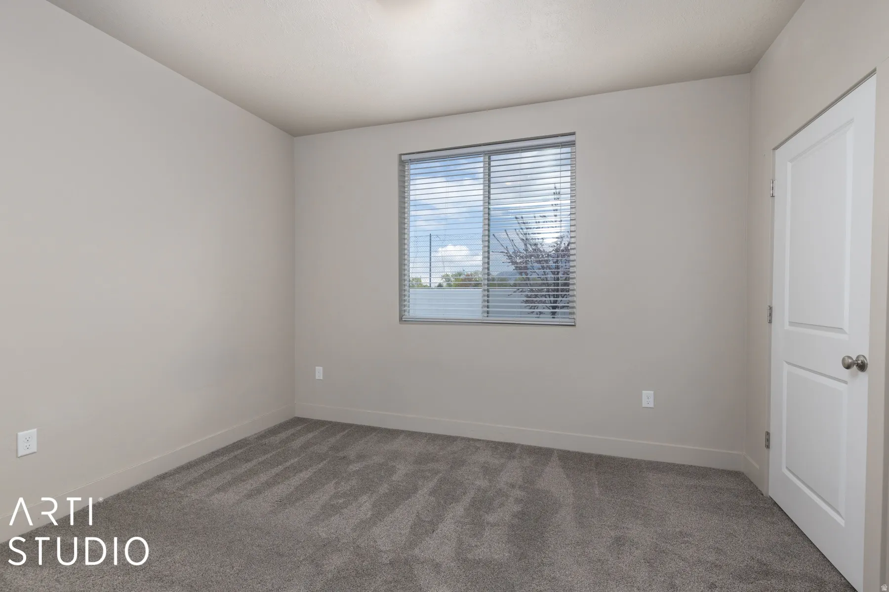 Room featuring neutral wall paint, gray carpet flooring, a window with horizontal blinds, a white interior door, and white trim