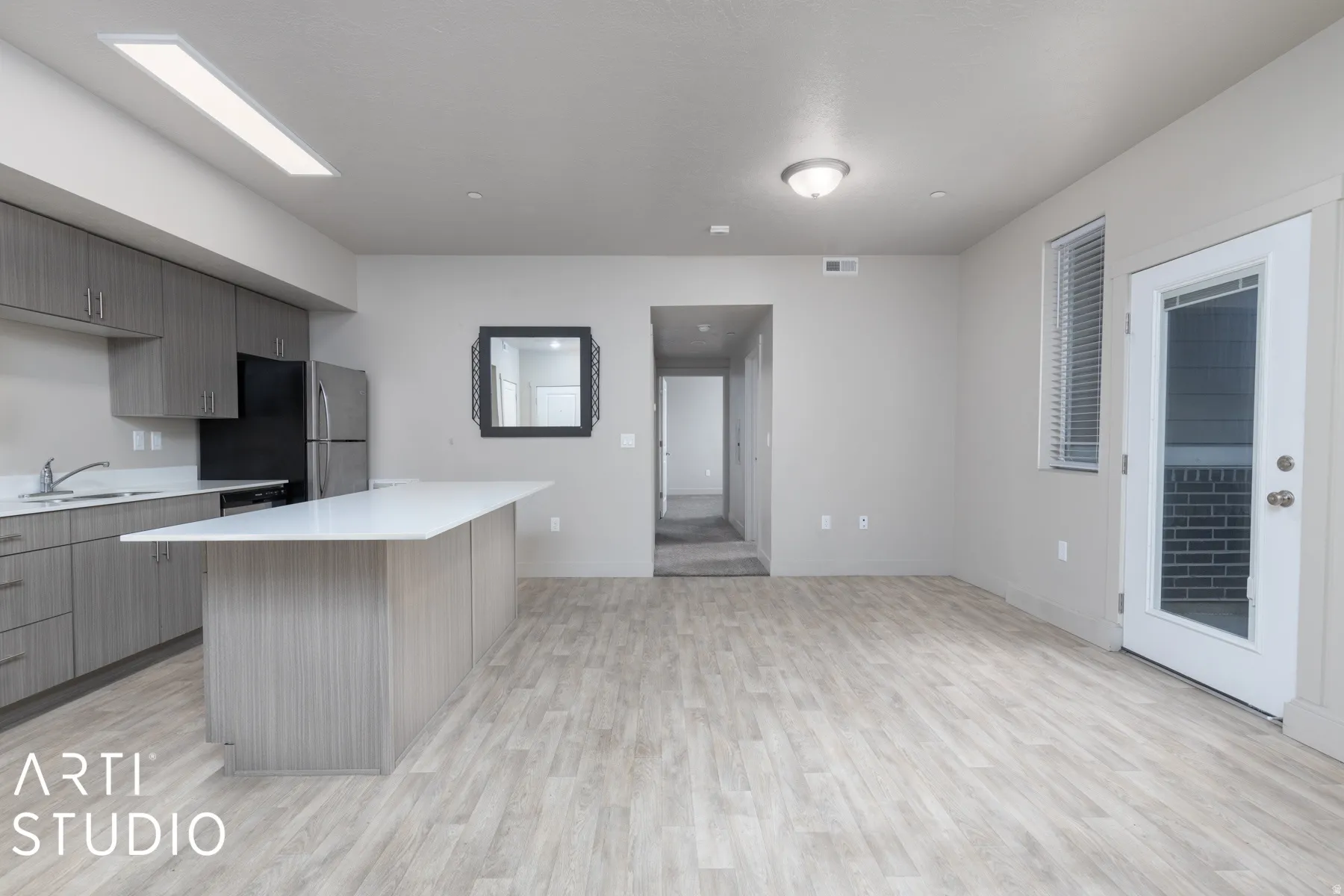 Open-concept living area featuring wood-finish flooring, a contemporary kitchen island with a light-colored countertop, and a fully equipped kitchen with stainless steel appliances and wood-grain cabinetry