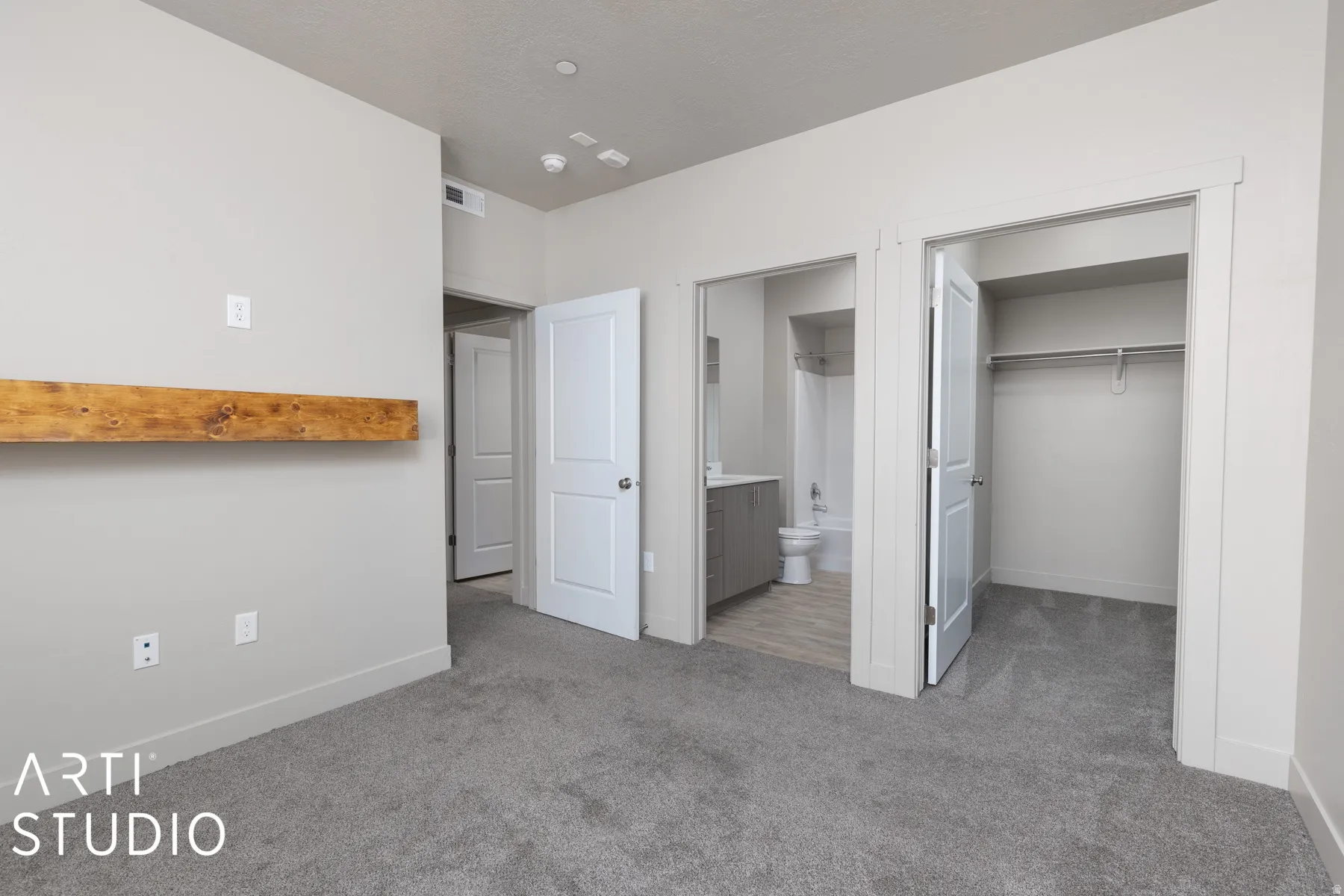 Carpeted bedroom featuring a floating wood shelf, an en-suite bathroom with a built-in vanity, and a closet with a built-in rod and shelf