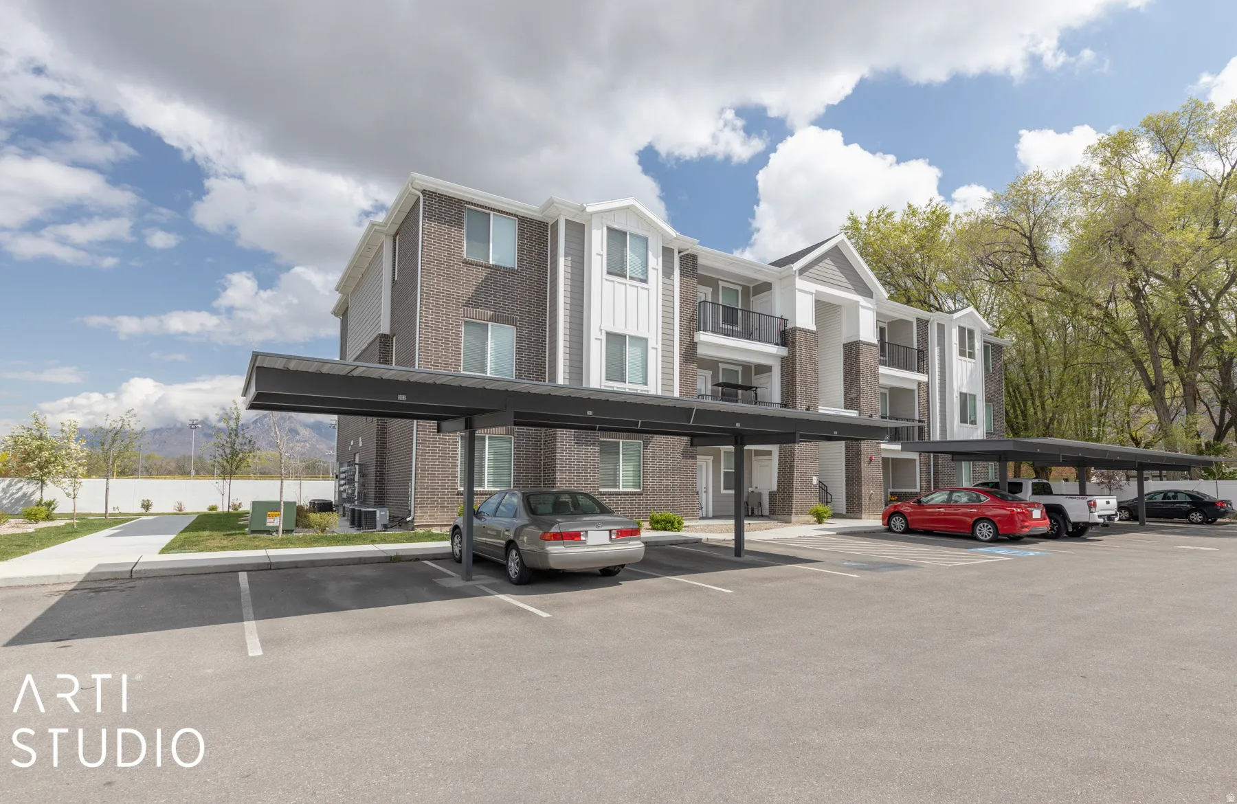 Multi-story building exterior featuring brick and siding accents, private balconies, and a covered parking area