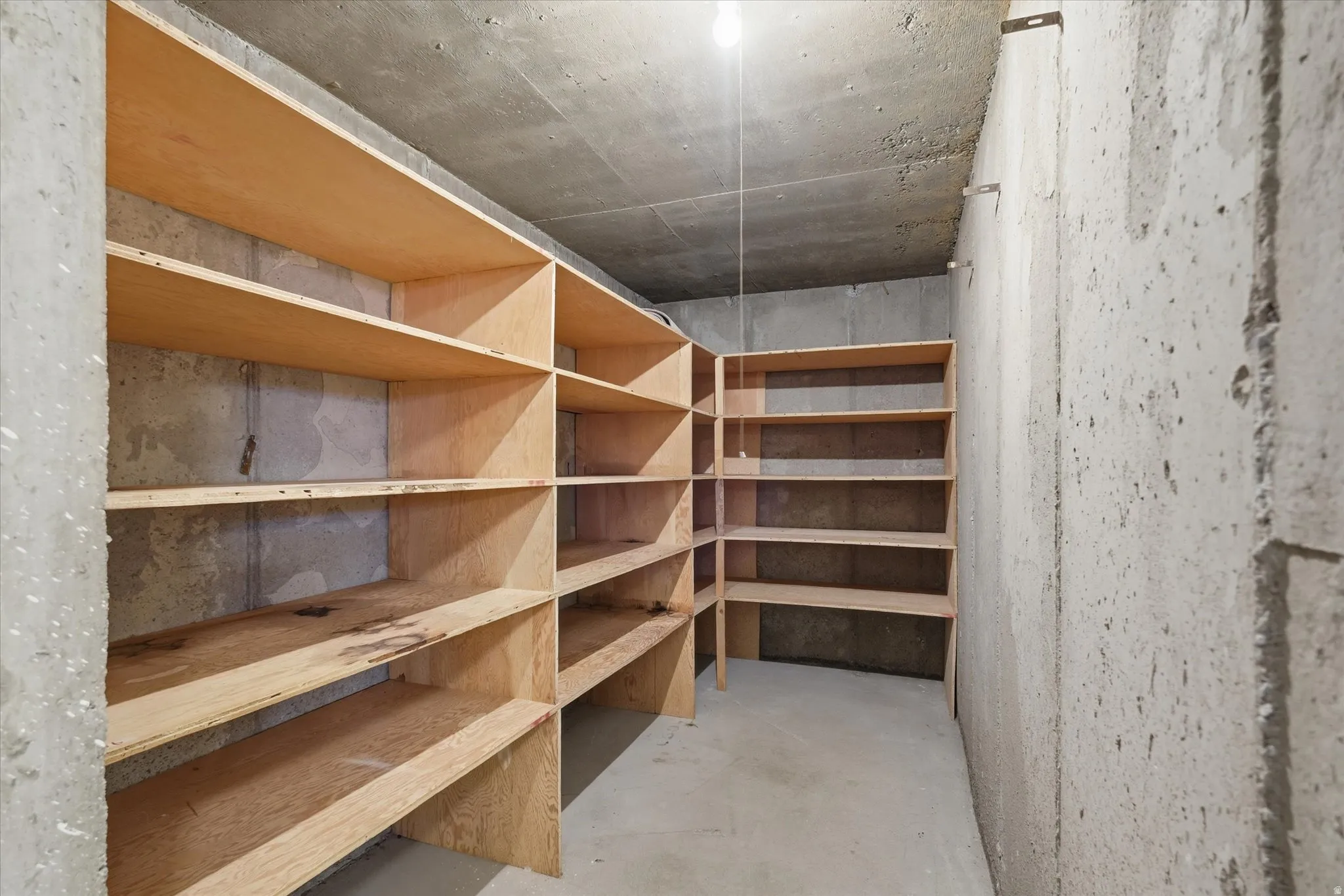 Concrete-walled storage area featuring extensive built-in wooden shelving
