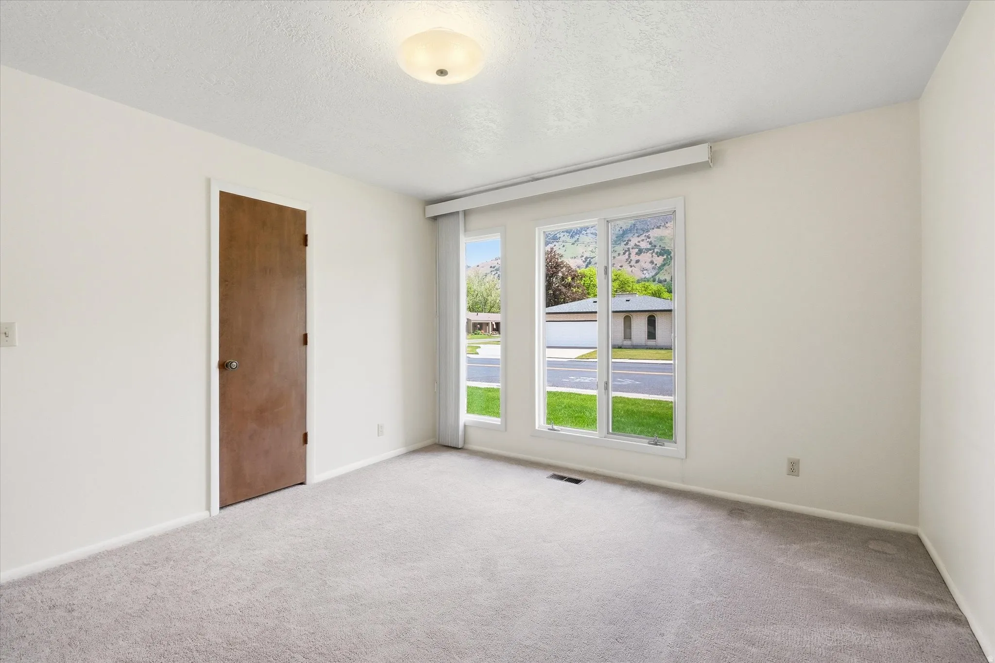 Bright room featuring three large windows, neutral wall paint, and grey carpeting