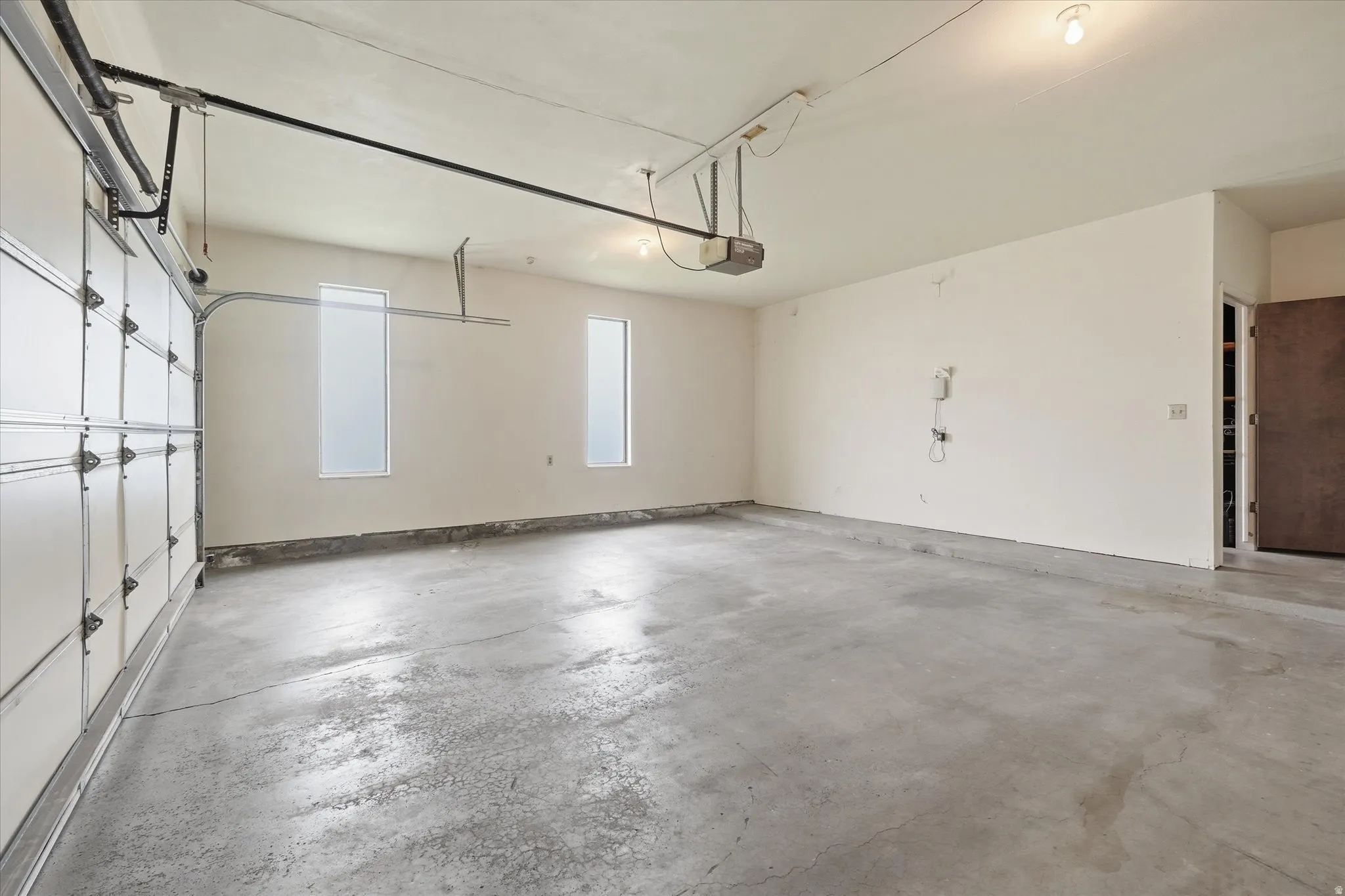 Spacious garage featuring a concrete floor, two vertical windows for natural light, and an overhead garage door opener mechanism
