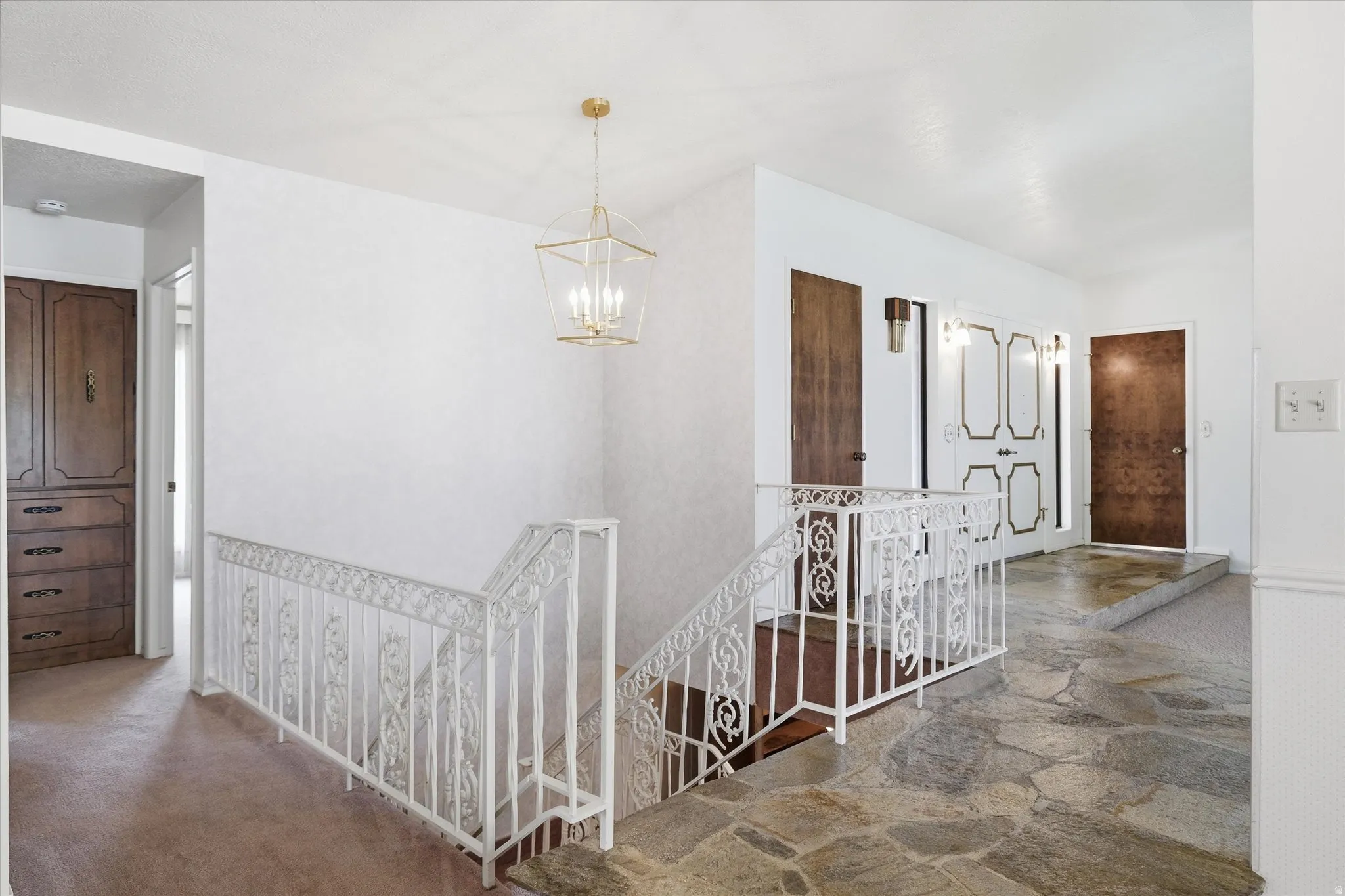 Flagstone flooring extending into the hallway, featuring a white wrought iron railing and a contemporary gold-finished chandelier