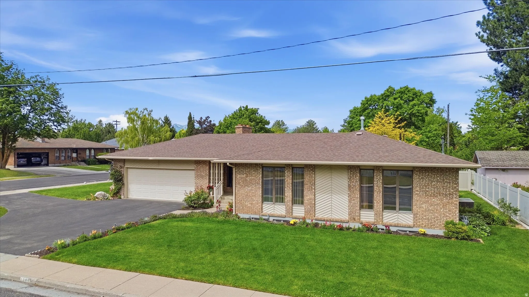 Brick exterior with a brown shingle roof, attached garage, paved driveway, and a manicured front lawn