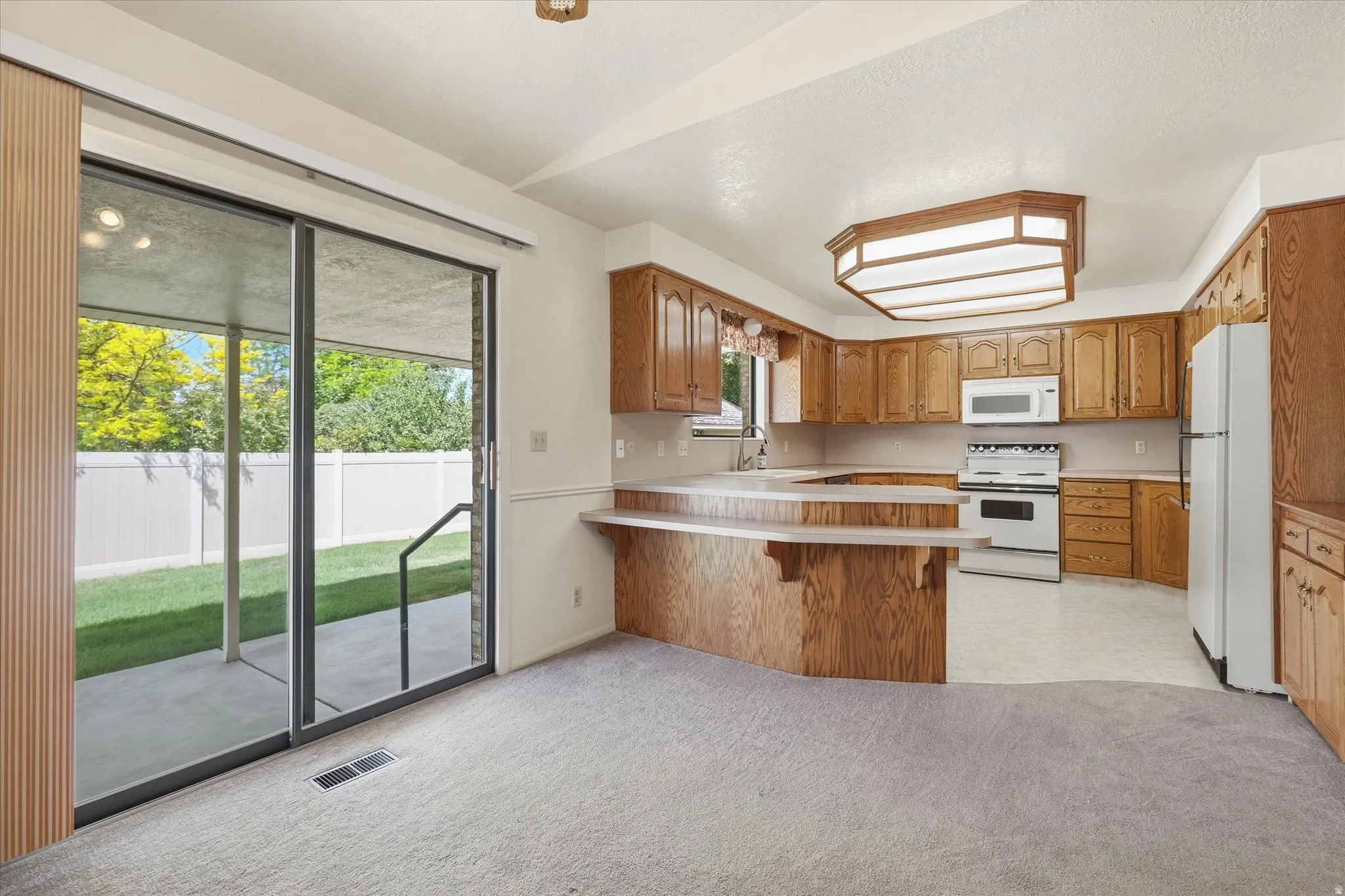 Kitchen with wood cabinetry and white appliances, featuring a breakfast bar