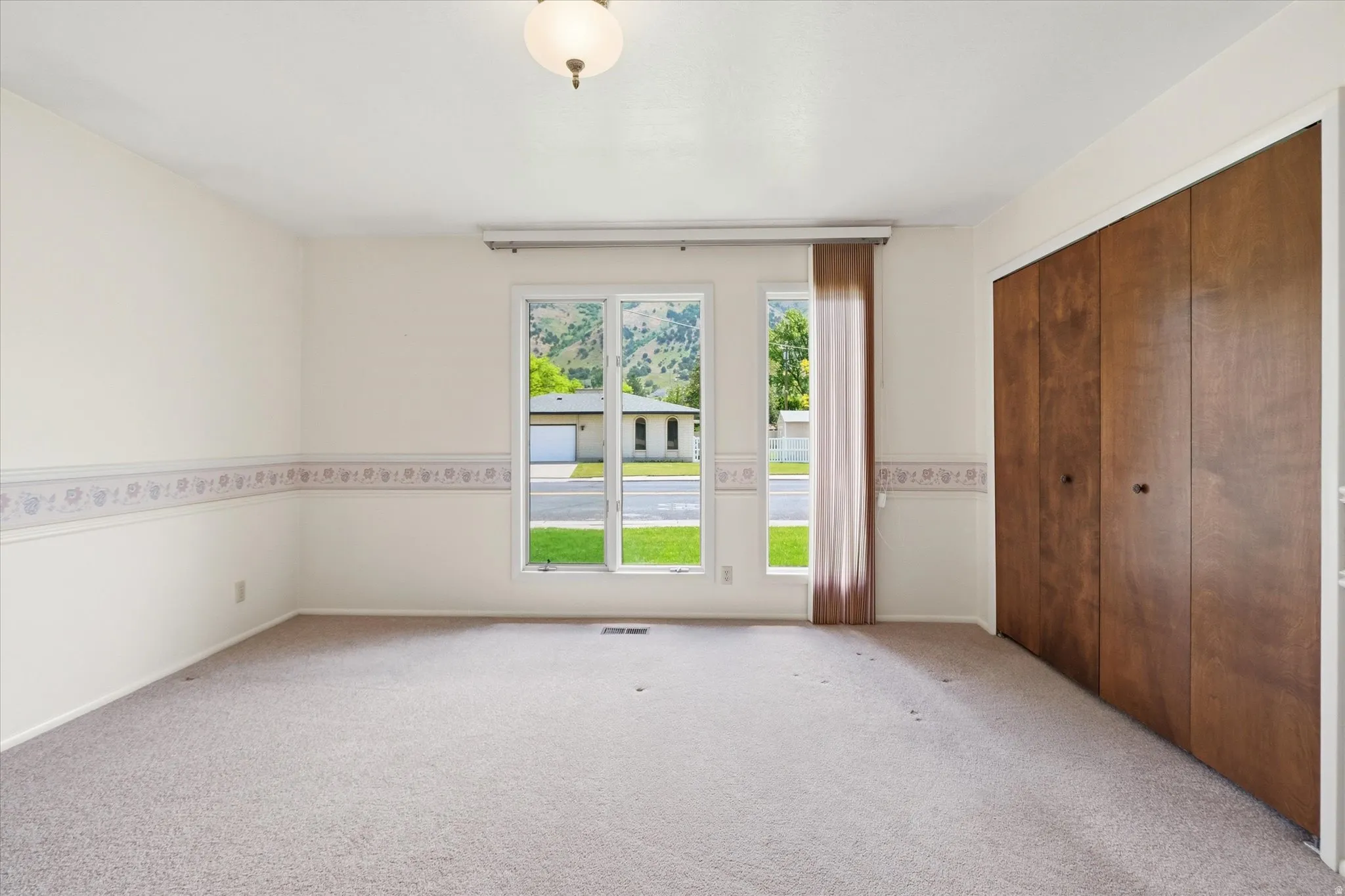Carpeted room featuring a large window, a ceiling-mounted light fixture, and a built-in closet with bi-fold doors