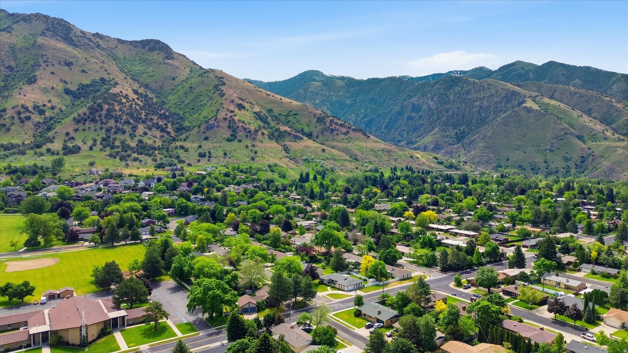 Expansive mountain landscape frames a verdant community with mature trees and residential properties