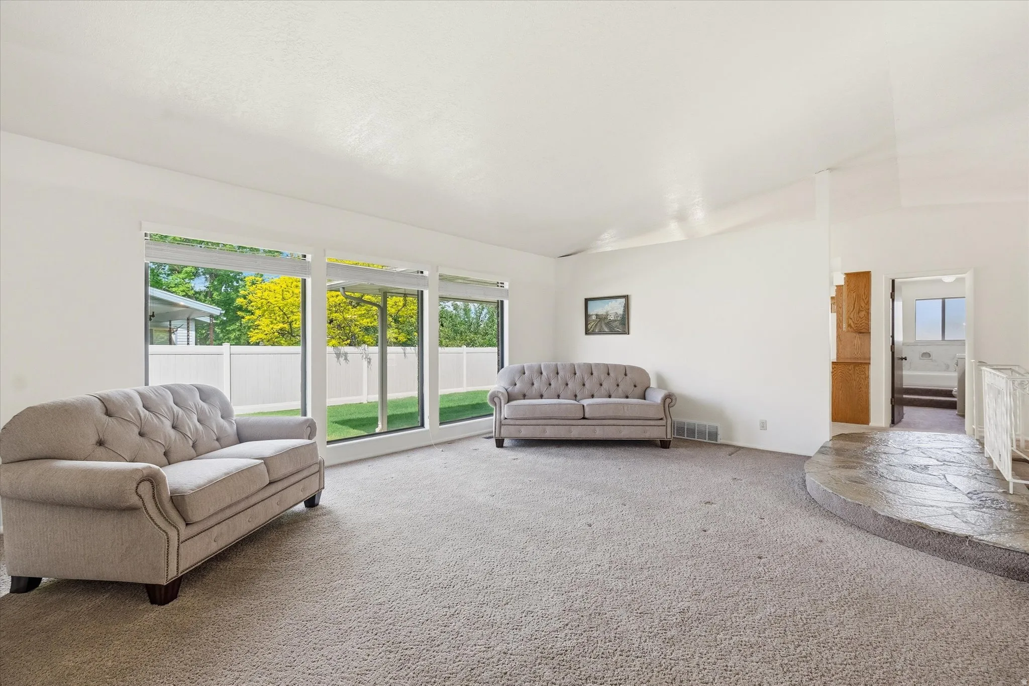 Spacious interior featuring large picture windows overlooking a fenced rear yard with mature trees