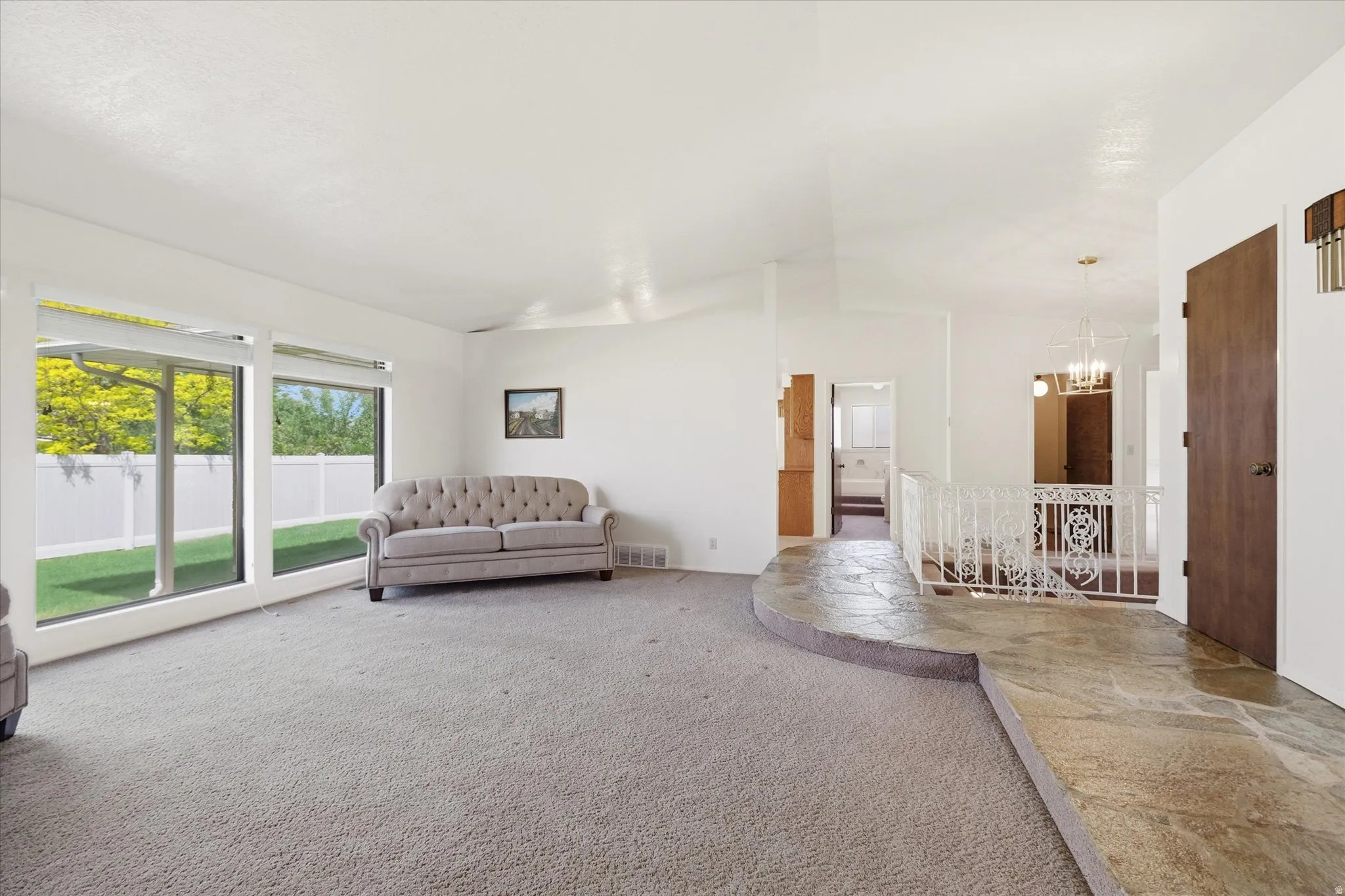 Spacious living area featuring large picture windows, vaulted ceilings, and light-toned carpeting