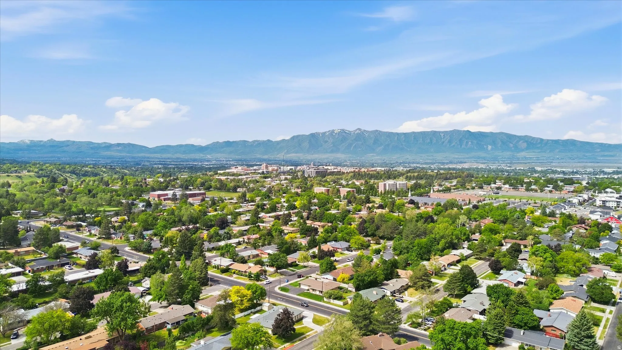 Aerial perspective showcasing a residential area with mature trees and a distant mountain range under a clear sky