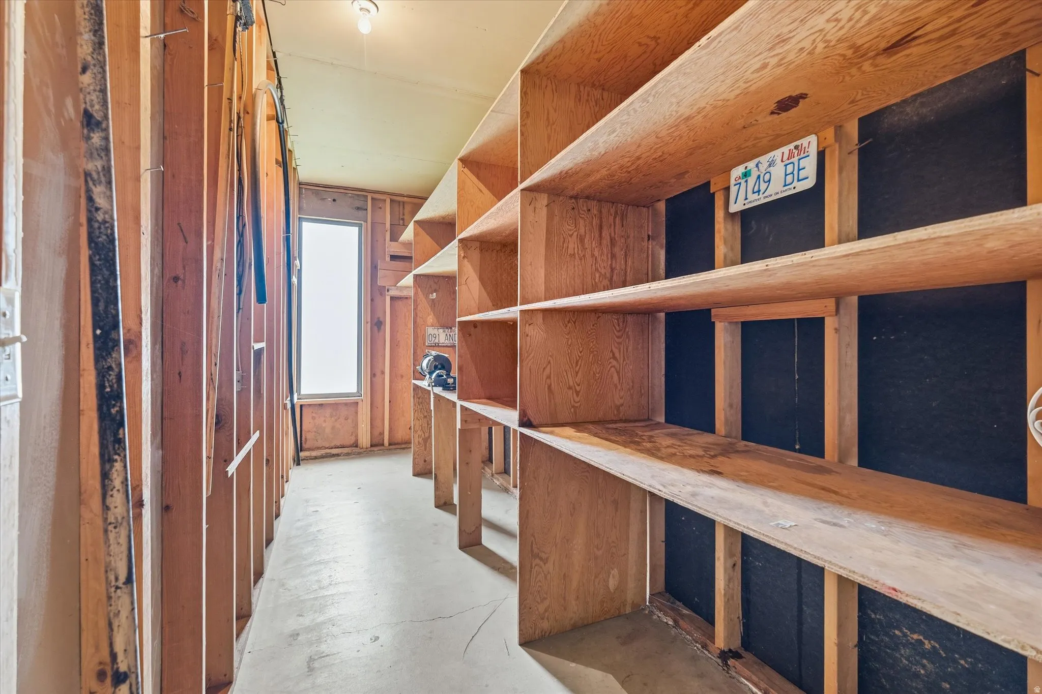 Utility room featuring extensive built-in wooden shelving, a single window, exposed wood framing, and concrete flooring