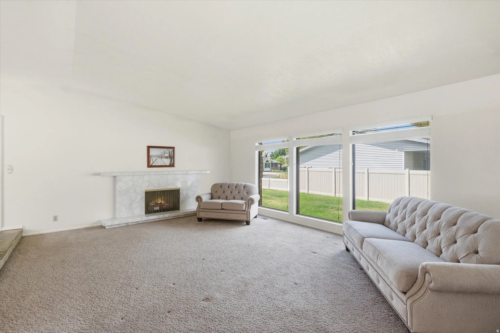 Spacious interior featuring a white-painted fireplace with a stone surround, a large picture window, and light-colored carpeting