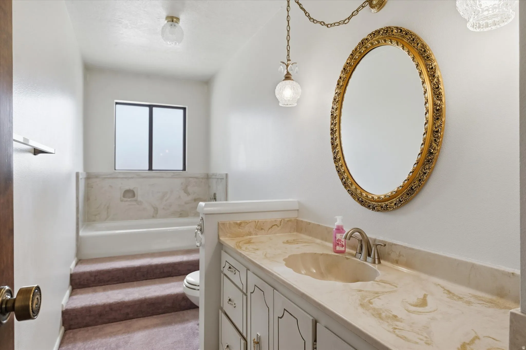 Vanity featuring a stone countertop with an integrated sink and a classic gold-framed mirror