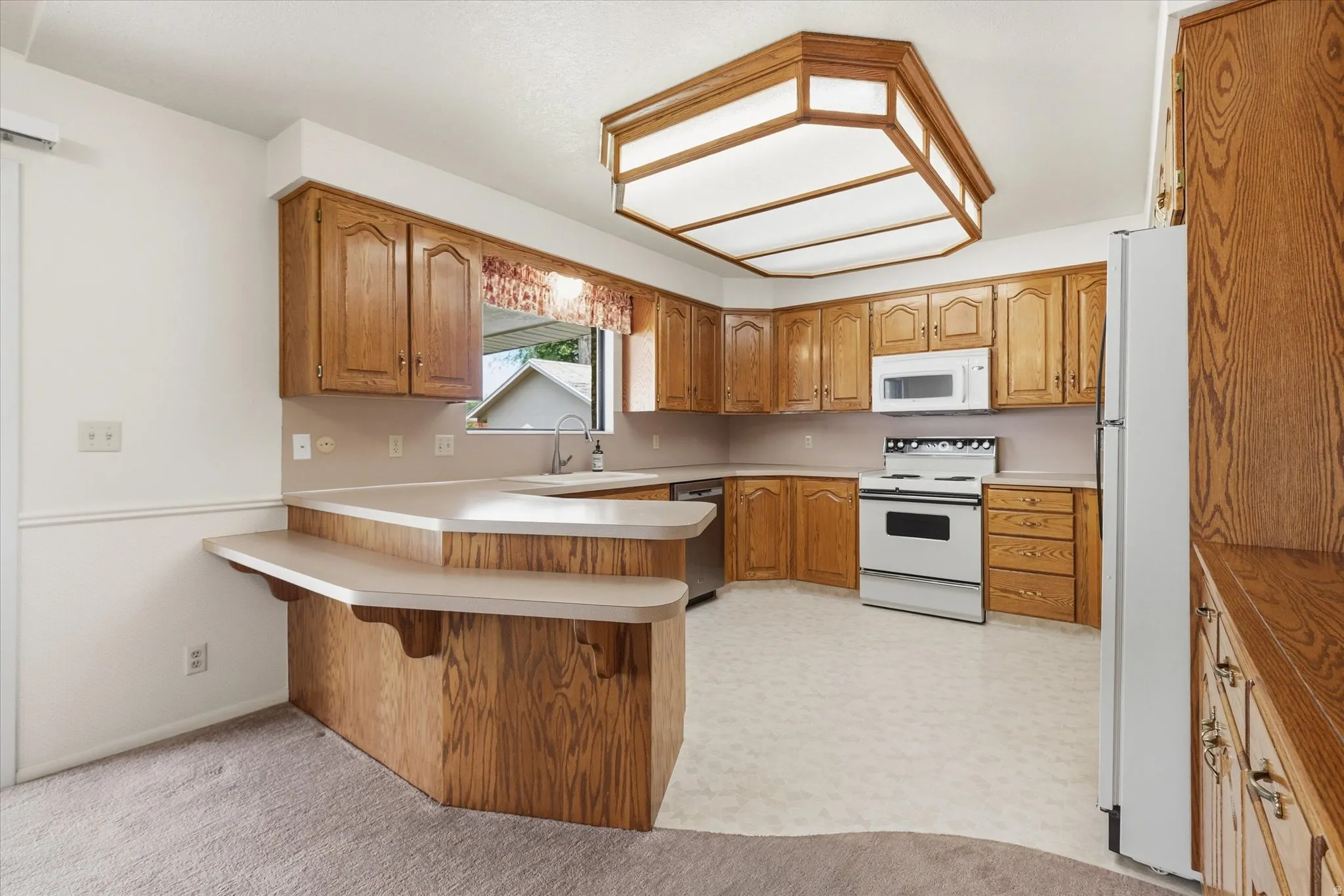 Kitchen featuring wood cabinetry, white appliances, a double-tiered breakfast bar, and a built-in ceiling light fixture