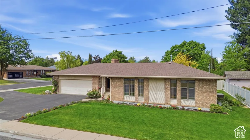 Brick exterior with a brown shingle roof, attached garage, paved driveway, and a manicured front lawn