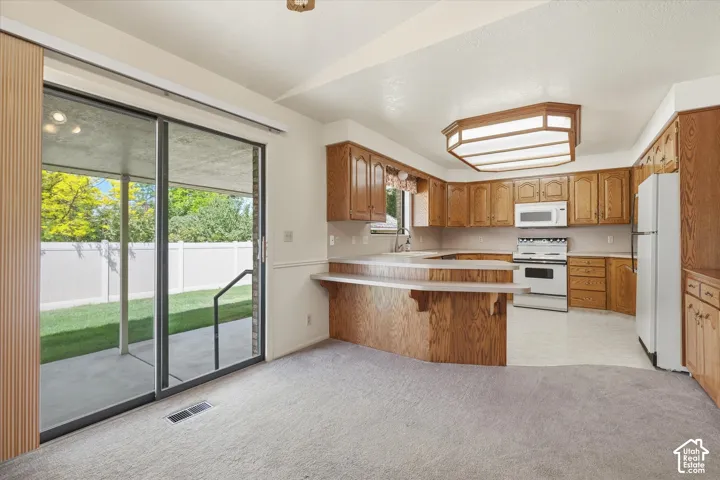 Kitchen with wood cabinetry and white appliances, featuring a breakfast bar