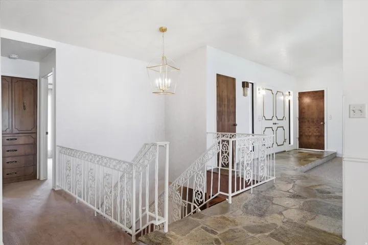 Flagstone flooring extending into the hallway, featuring a white wrought iron railing and a contemporary gold-finished chandelier